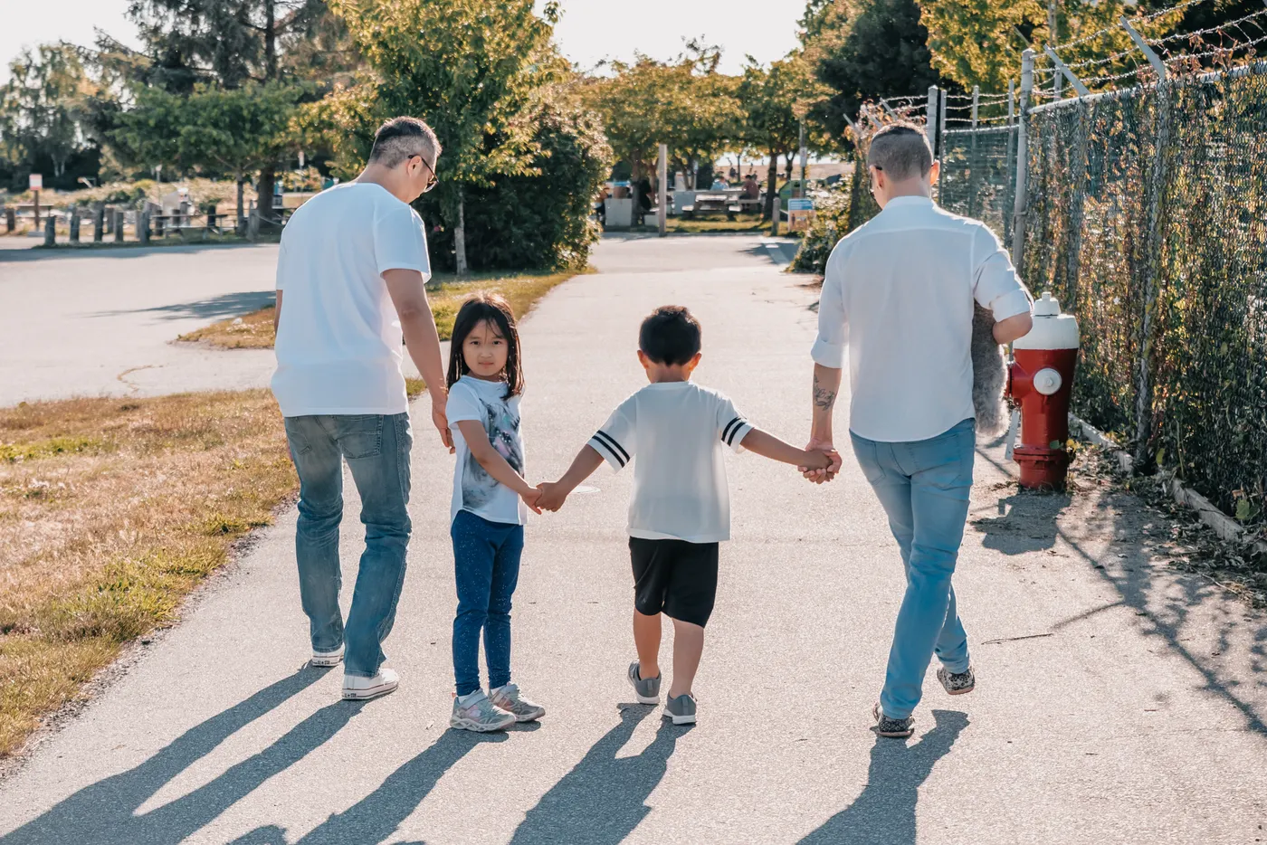 Two adults and two children walking hand in hand along a sidewalk.